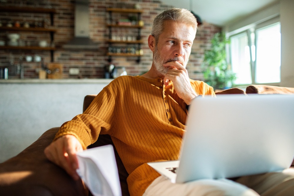 A man in his 50s thinking while using a laptop